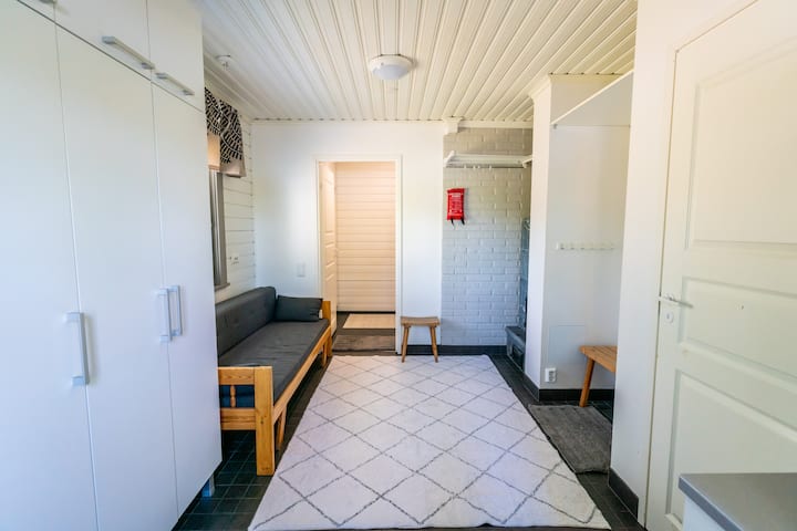 Tämä on kodinhoitohuone. Kuvassa olevat sohva on vuodesohva, joka aukeaa 140 cm leveäksi varavuoteeksi. Sohvalla voi nukkua enintään 2 henkilöä. Sohvaa vastapäätä on takka. Täältä on pääsy WC-, suihku- ja saunatiloihin.