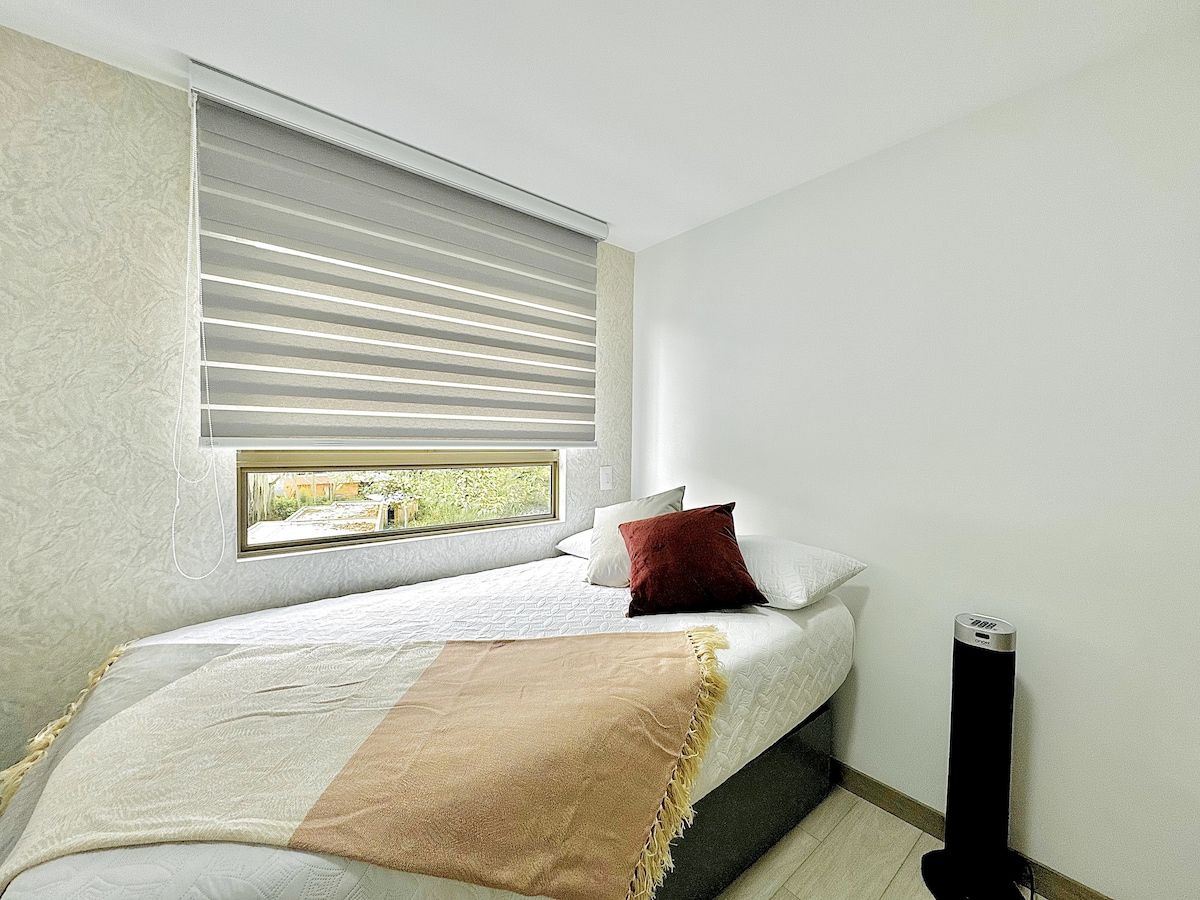 Svijetla soba s bračnim krevetom, uređena mekim tonovima i ukrasnim jastucima. Prozor pruža hladnu i prozračnu atmosferu, a ventilator savršeno nadopunjuje udobnost prostora.