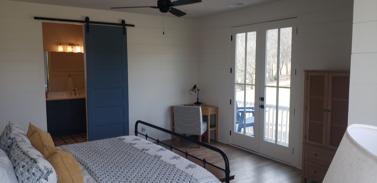 Лизгачка врата од бања со двојни мијалници и голем туш.  Биро во аголот за тивок работен простор.  Француските врати водат до балкон. 