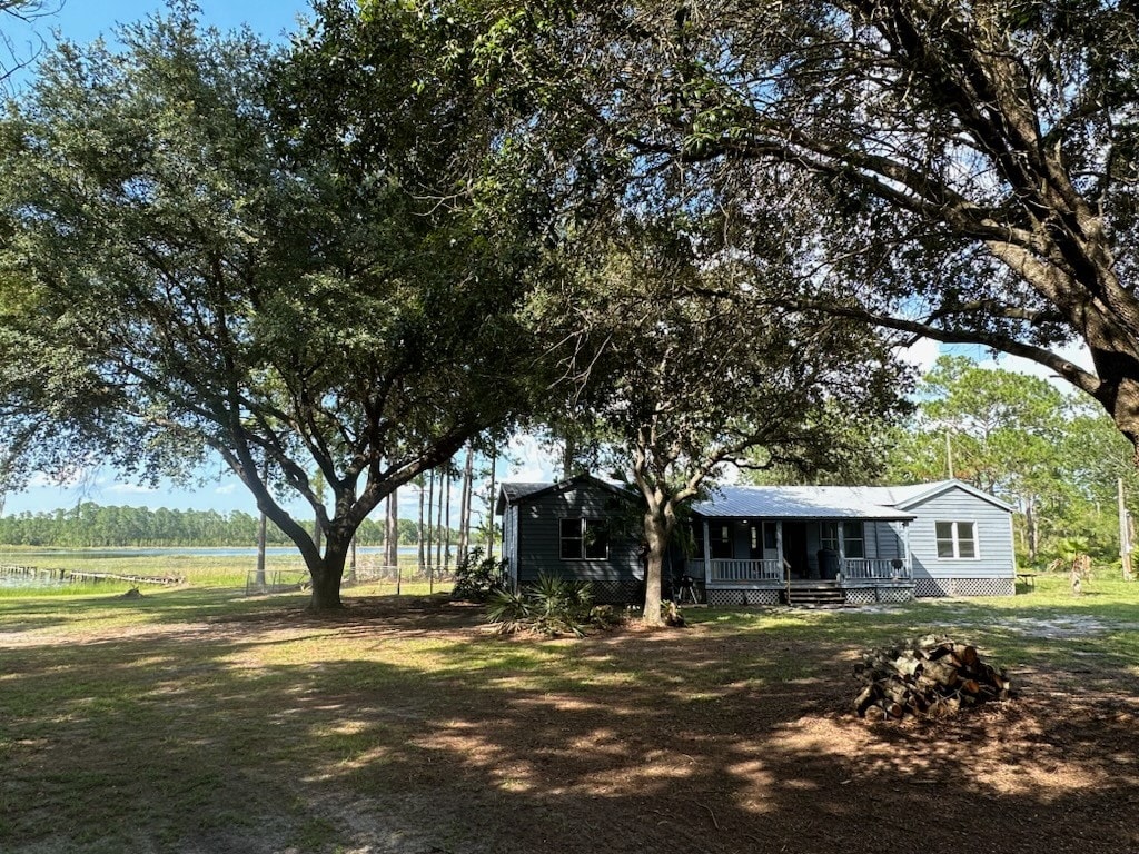 The exterior of a spacious home is shown, nestled among large trees that provide ample shade. A smooth pathway leads to the entrance, while a grassy area surrounds the house, offering a serene atmosphere with views of the distant lake and surrounding nature.