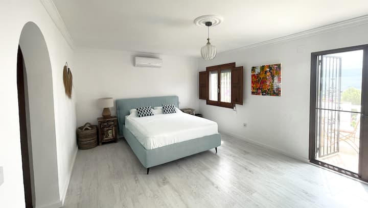 Დელუქს ‑ კლასის საწოლი, რომელიც მოთავსებულია პრემიუმ კლასის ღია ცისფერი ნაცრისფერი თეთრეულის ქსოვილში. Თეთრი გარეცხილი ნაცრისფერი თეთრი იატაკი, ბროლის გულსაკიდი განათება, კონდიციონერი და ორი ხელნაკეთი საწოლისპირა მაგიდა ლამპით.