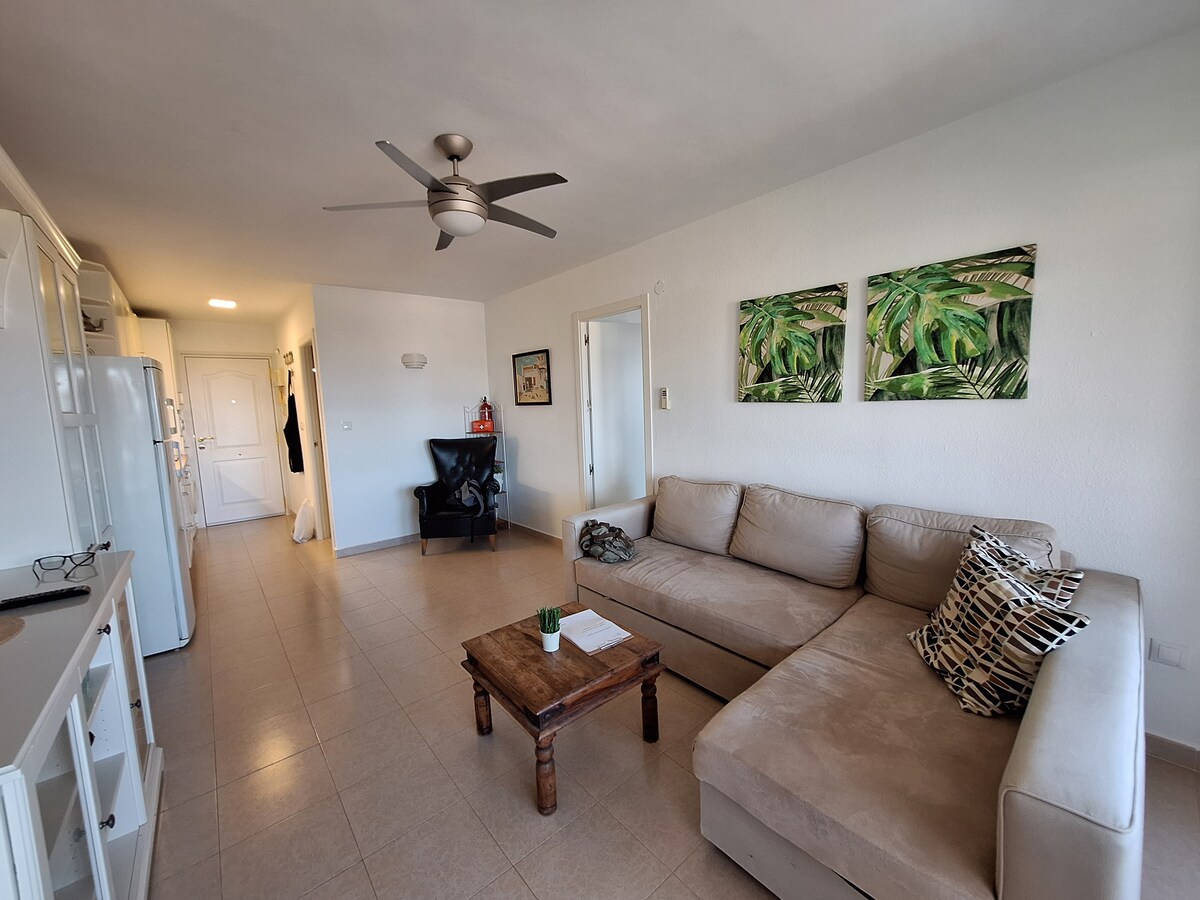 разтегателен диван, масичка за кафе, маса, столове, телевизор, вентилатор на тавана, голям подов вентилатор, фотьойл, климатик