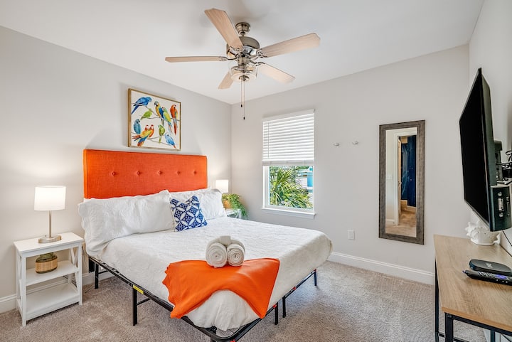 [Bedroom, Upstairs] 

Happy and inviting upstairs bedroom featuring a vibrant orange headboard, Roku-enabled TV, and comfortable linens. Plus, a dedicated workspace for remote workers ensures you can stay productive while enjoying your beach retreat!