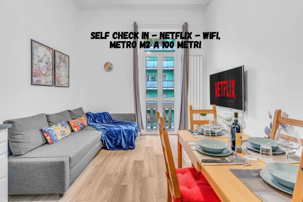 A living area features a gray sofa adorned with colorful cushions and a cozy blanket. A wooden dining table is set for four, ready for meals, while a large TV displays the Netflix logo. A balcony is visible through a brightly lit window.