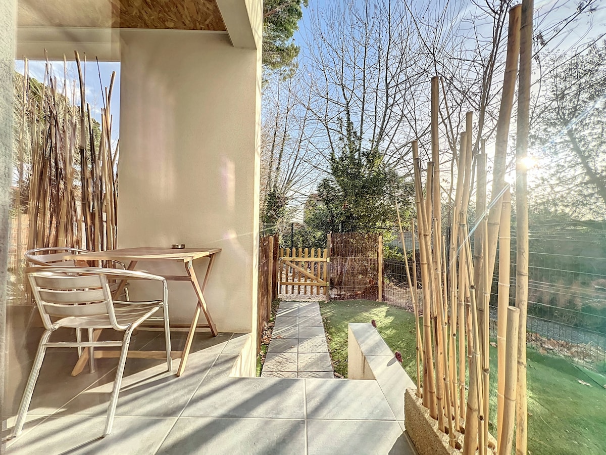 A private terrace is featured, bordered by slender bamboo plants. A simple outdoor table with two chairs is positioned on sleek tiles, providing a peaceful view of the garden. Natural light streams in, highlighting the tranquil setting.