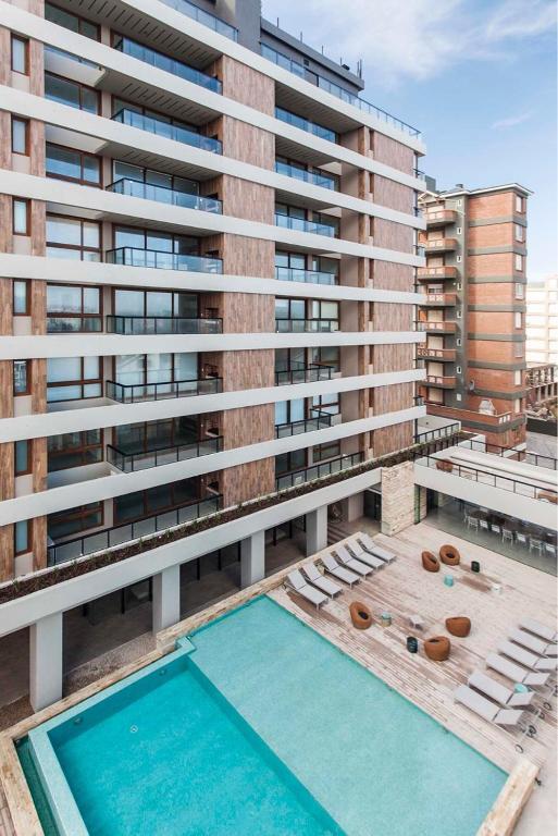 An outdoor pool is surrounded by lounge chairs on a sun deck, providing a space for relaxation. The building's architecture features a combination of wood and glass elements. Balconies are visible on multiple floors, offering an inviting view of the pool area.