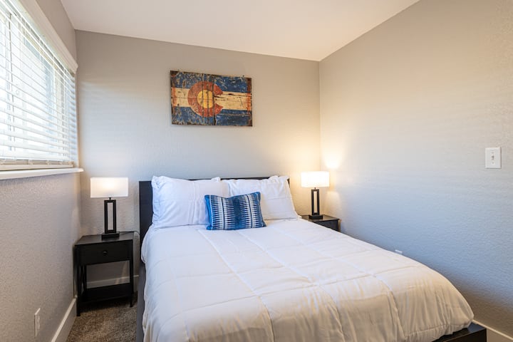 سرير بحجم كوين في أصغر ثلاث غرف نوم كاملة الحجم مع طاولتين طرفيتين ومصابيح بجانب السرير. 