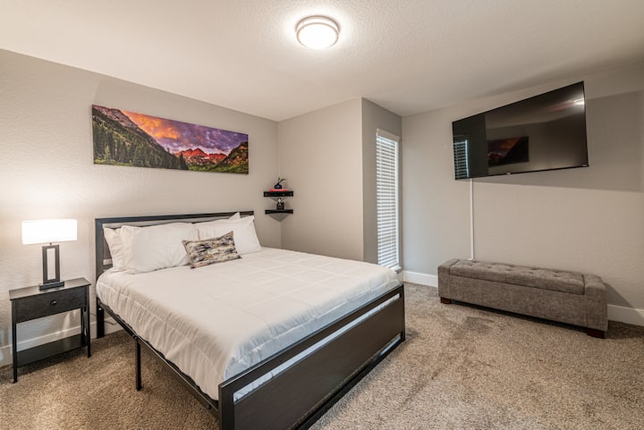 سرير بحجم كبير في غرفة النوم الرئيسية مع تلفزيون ذكي كبير ومقعد. طاولة بجانب الليل مع إضاءة بجانب السرير. 