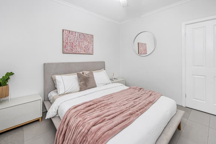 Luminoso y acogedor: el dormitorio rosa cuenta con una cómoda cama tamaño queen de lino de Freedom y grandes mesitas de noche, con vistas serenas a la terraza.