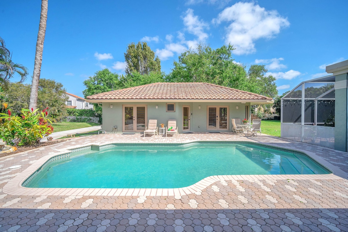 A peaceful outdoor area features a refreshing pool surrounded by a paved patio. Lounge chairs are positioned near the water, offering a space for relaxation. Lush greenery and trees provide a tranquil backdrop, enhancing the serene atmosphere in this private setting.