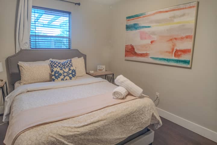 Bedroom with rolled towels, nailhead headboard & abstract wall art — includes dual nightstands, blackout blinds, and cozy bedding for guest-ready comfort