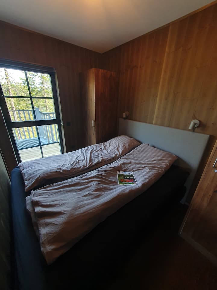 Dormitorio rústico con paredes oscuras, cama grande con edredones separados, luz natural y vistas al balcón.