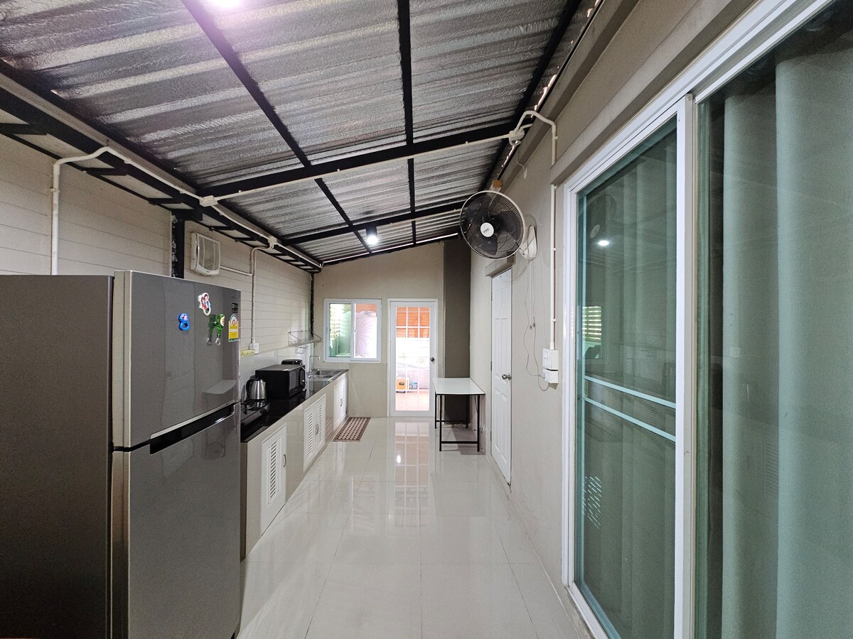 A modern kitchen is equipped with stainless steel appliances, including a refrigerator and a gas stove. Sleek countertops provide ample workspace, while large windows allow natural light to fill the area. A fan is mounted on the ceiling to enhance air circulation.