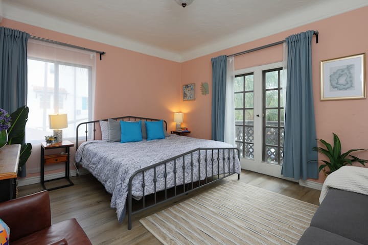 Encantador dormitorio con una cama tamaño king, suave pared decorativa de color rosa y toques de azul vibrante.