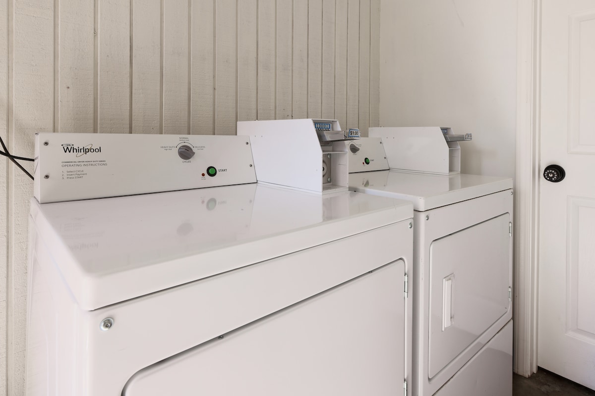 A laundry room is equipped with Whirlpool washer and dryer units, featuring a clean and minimalist design. The devices are positioned side by side, with clear control panels visible, facilitating easy operation for guests during their stay.