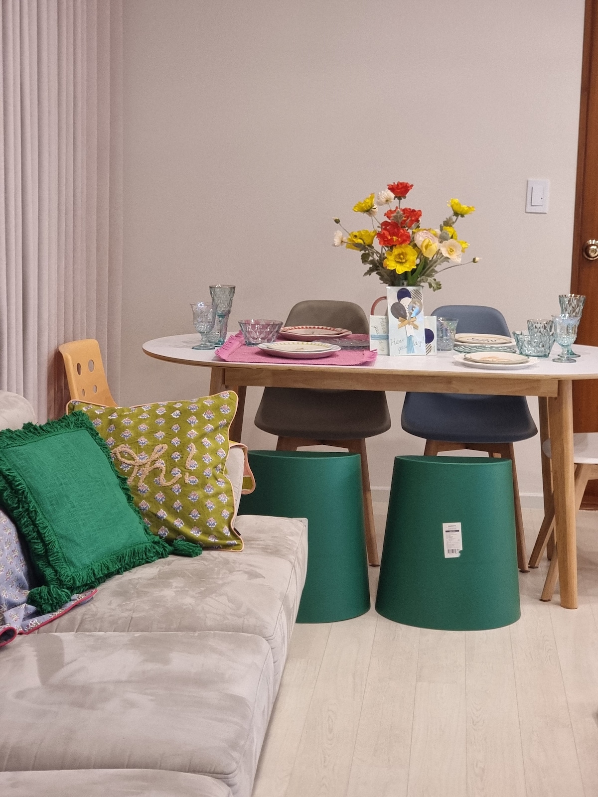 A dining area is showcased, featuring a round table set with colorful plates and glassware. A floral centerpiece adds vibrancy. Nearby, a soft couch with decorative pillows complements the space, while modern chairs surround the table, creating an inviting atmosphere for meals.