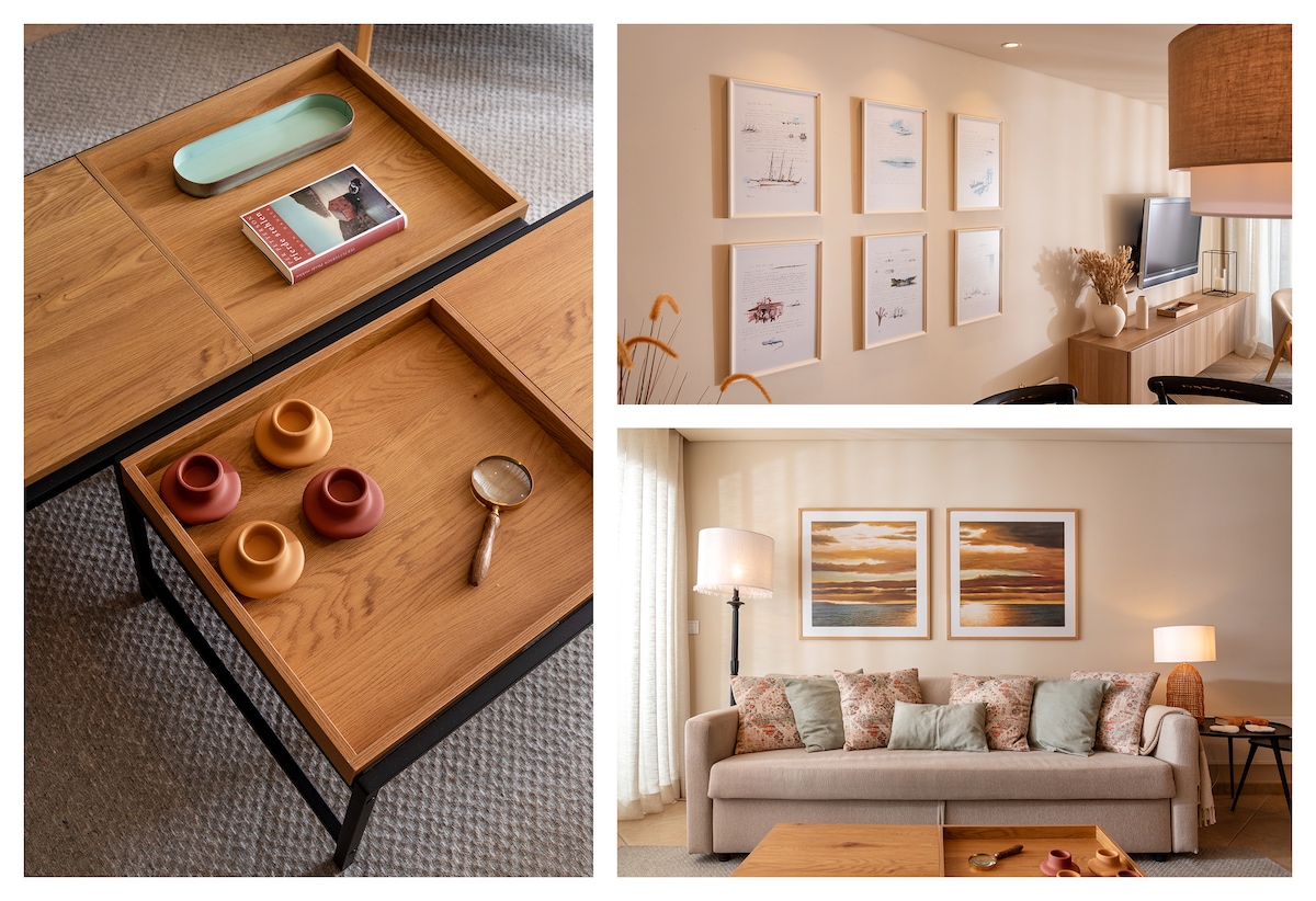 An elegant wooden coffee table features two trays, one with a pale blue dish and another with colored cups. A wall displays framed artwork and a small decorative vase. A light-colored sofa with decorative pillows faces a television, complemented by a standing lamp.