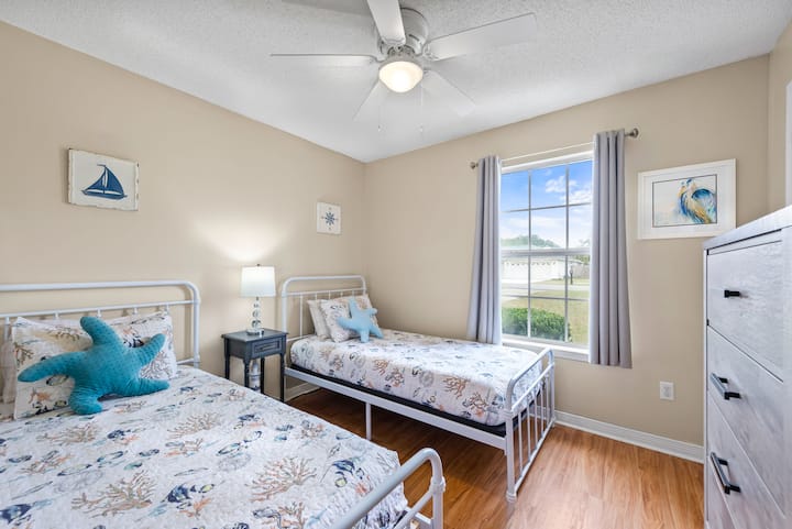 Cozy bedroom with two twin beds, a center table with lamp, and room-darkening curtains — perfect for kids, friends, or extra guests seeking comfort and privacy