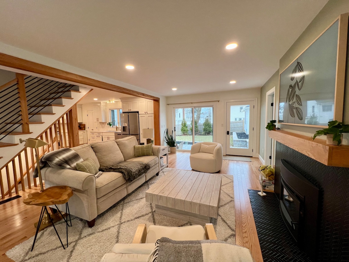 A comfortable living area is highlighted by a light-colored sectional sofa and a large, textured area rug. A modern coffee table sits in the center. Natural light floods the space through sliding glass doors leading to the backyard, creating a bright and inviting ambiance.