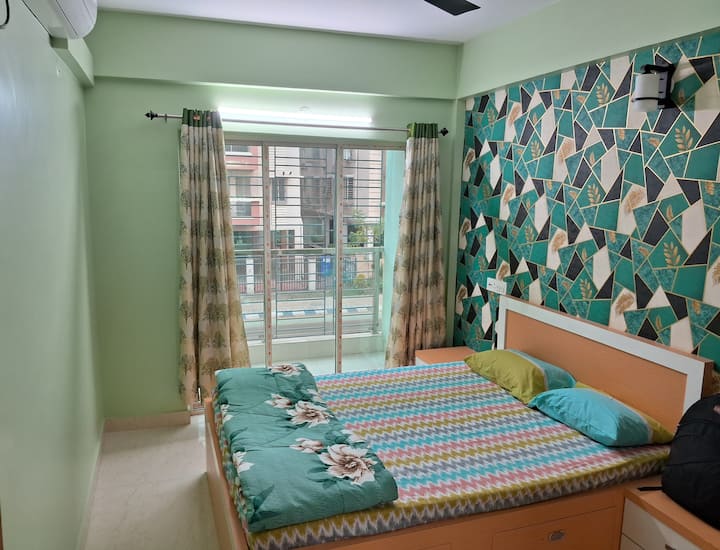 设备齐全的空调卧室，带阳台，包括床、衣柜、分体式空调、风扇、照明以及舒适的床上用品和装饰，营造出一个放松的空间。