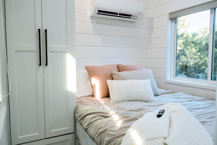 The bedroom is a comfy retreat that boasts a hybrid memory foam queen size mattress with luxurious bedding and lots of fluffy pillows. Unlike most tiny homes, the bedroom is on the main floor so you don't have to climb a ladder to get to it. 