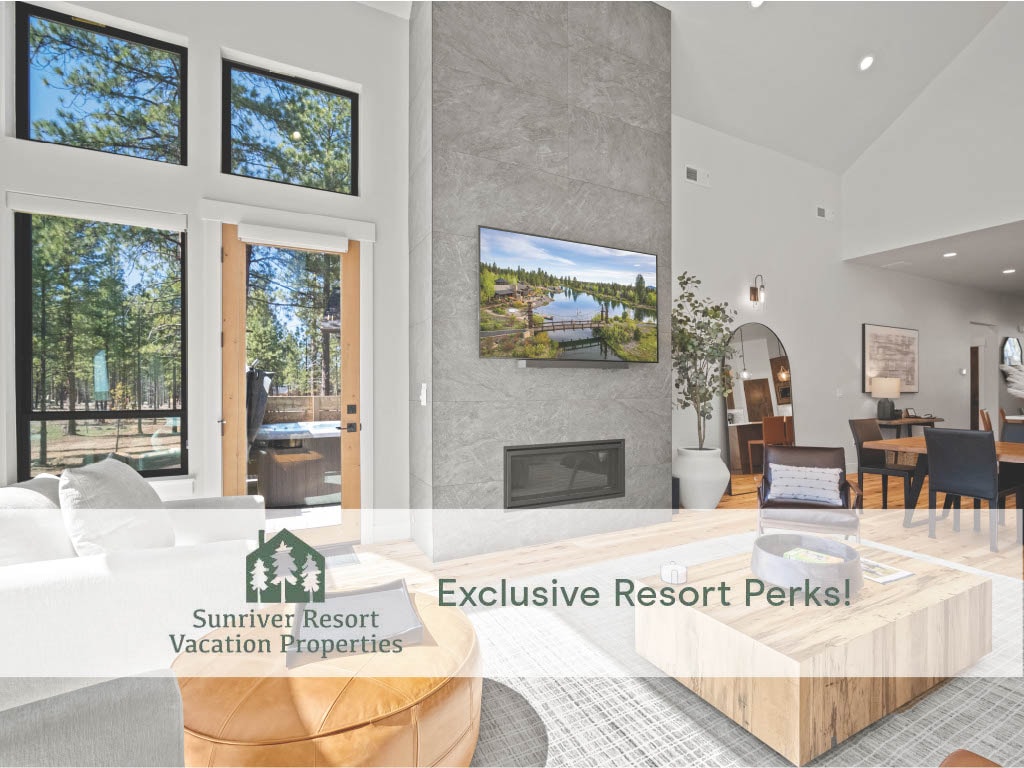A spacious living area is highlighted by floor-to-ceiling windows, providing views of surrounding trees. A contemporary gas fireplace sits beneath a mounted TV, and a round coffee table is positioned on a light-colored rug. Dining and additional seating areas are visible in the background.