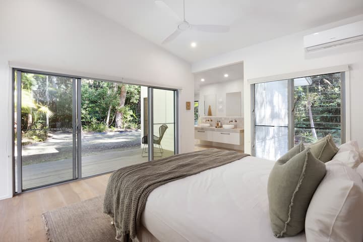 استمتع بالنوم في سرير كينج في غرفة النوم الرئيسية مع إطلالات على الأشجار، والوصول المباشر إلى الخارج والراحة من تكييف الهواء ومراوح السقف.