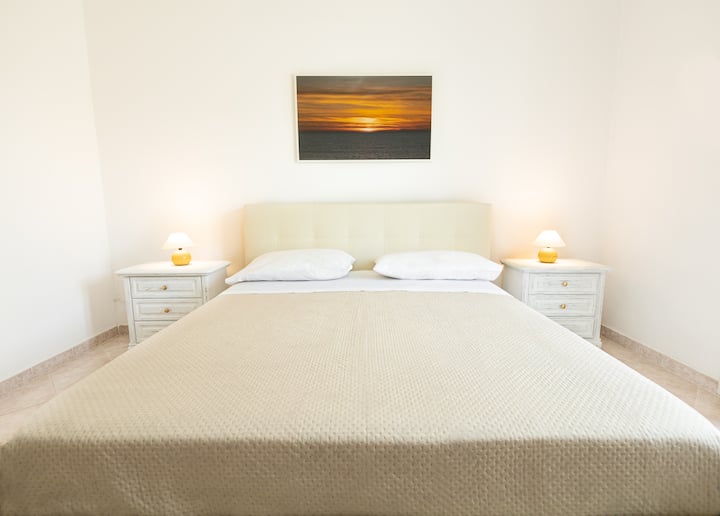 Dettaglio camera matrimoniale con letto King Size e vista sul giardino riservato. Dotata di smart tv, armadio con grucce appendiabiti e cassetti, comodini e cassettiera 