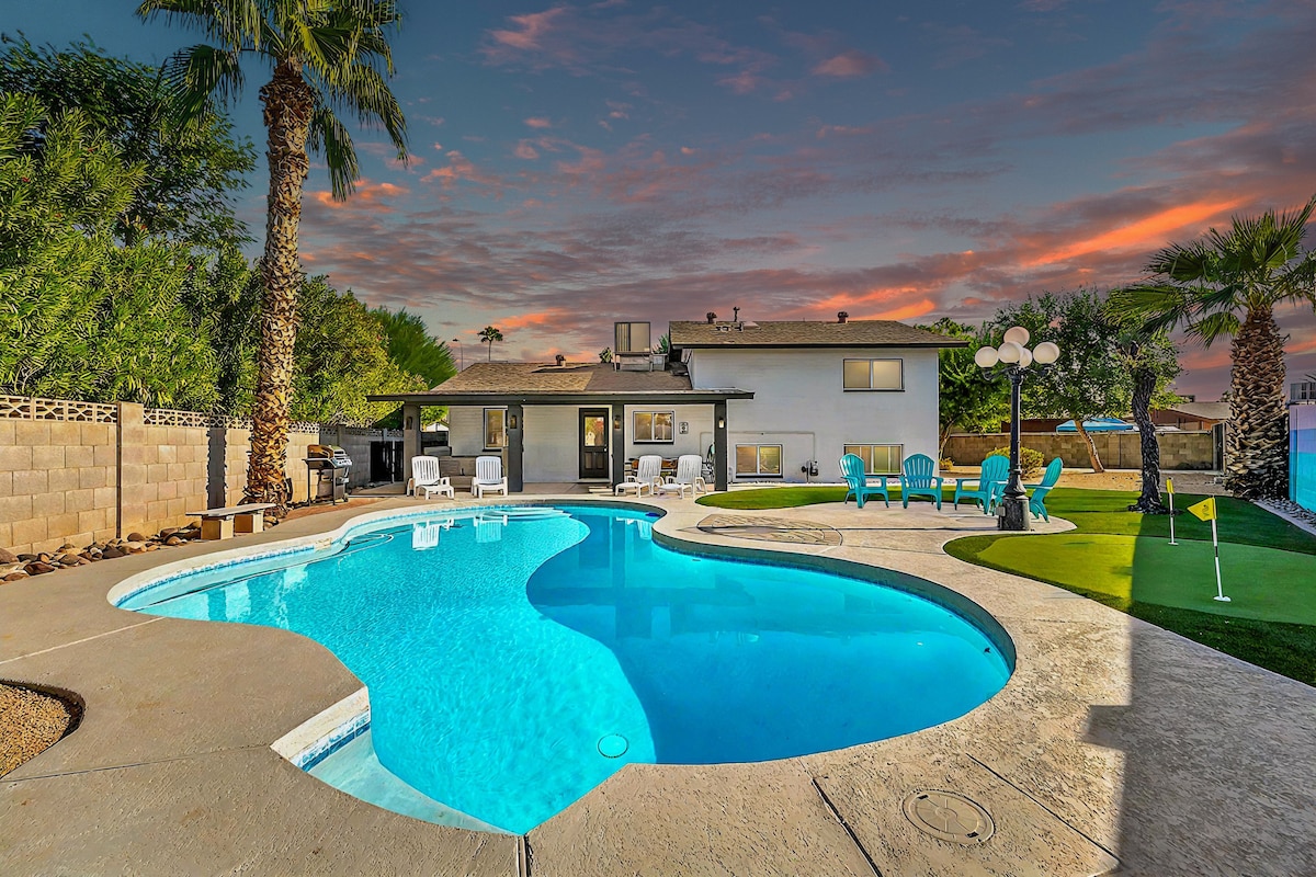 A private backyard is showcased, featuring a uniquely shaped pool surrounded by lounge chairs. Palm trees frame the area, while a putting green adds a recreational touch. Sliding doors from the house offer direct access, complementing the tranquil outdoor setting.