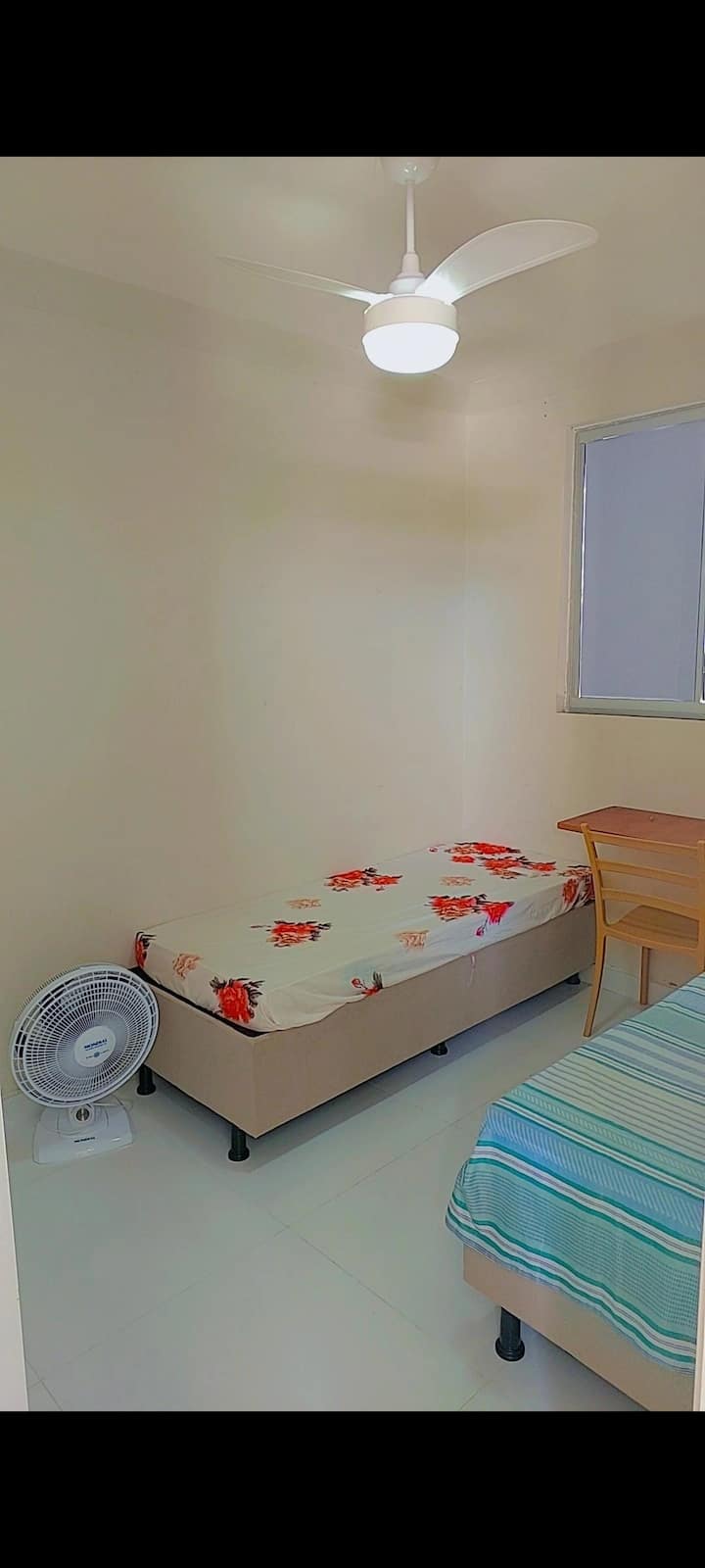 Chambre avec 2 lits simples, table de bureau, ventilateur de plafond et armoire. 