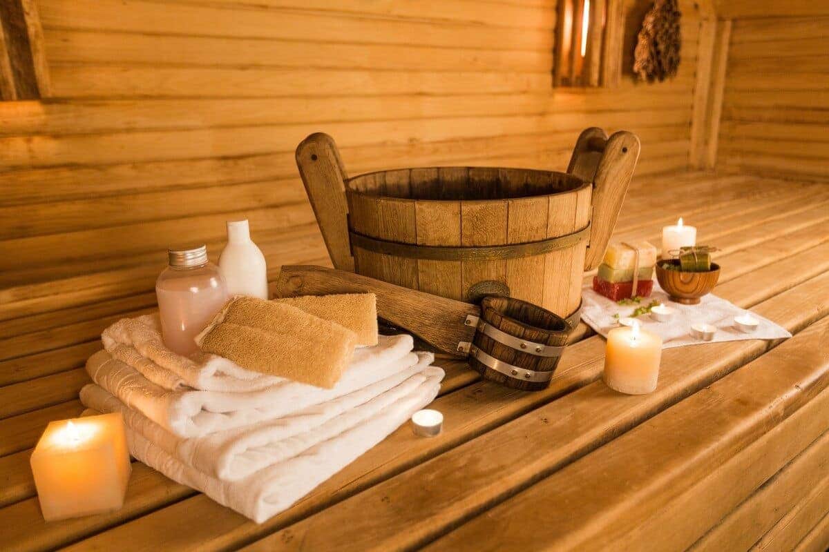 A wooden sauna interior features a rustic barrel, accompanied by neatly arranged towels, skincare products, and candles. The warm lighting enhances the cozy atmosphere, inviting relaxation and self-care.