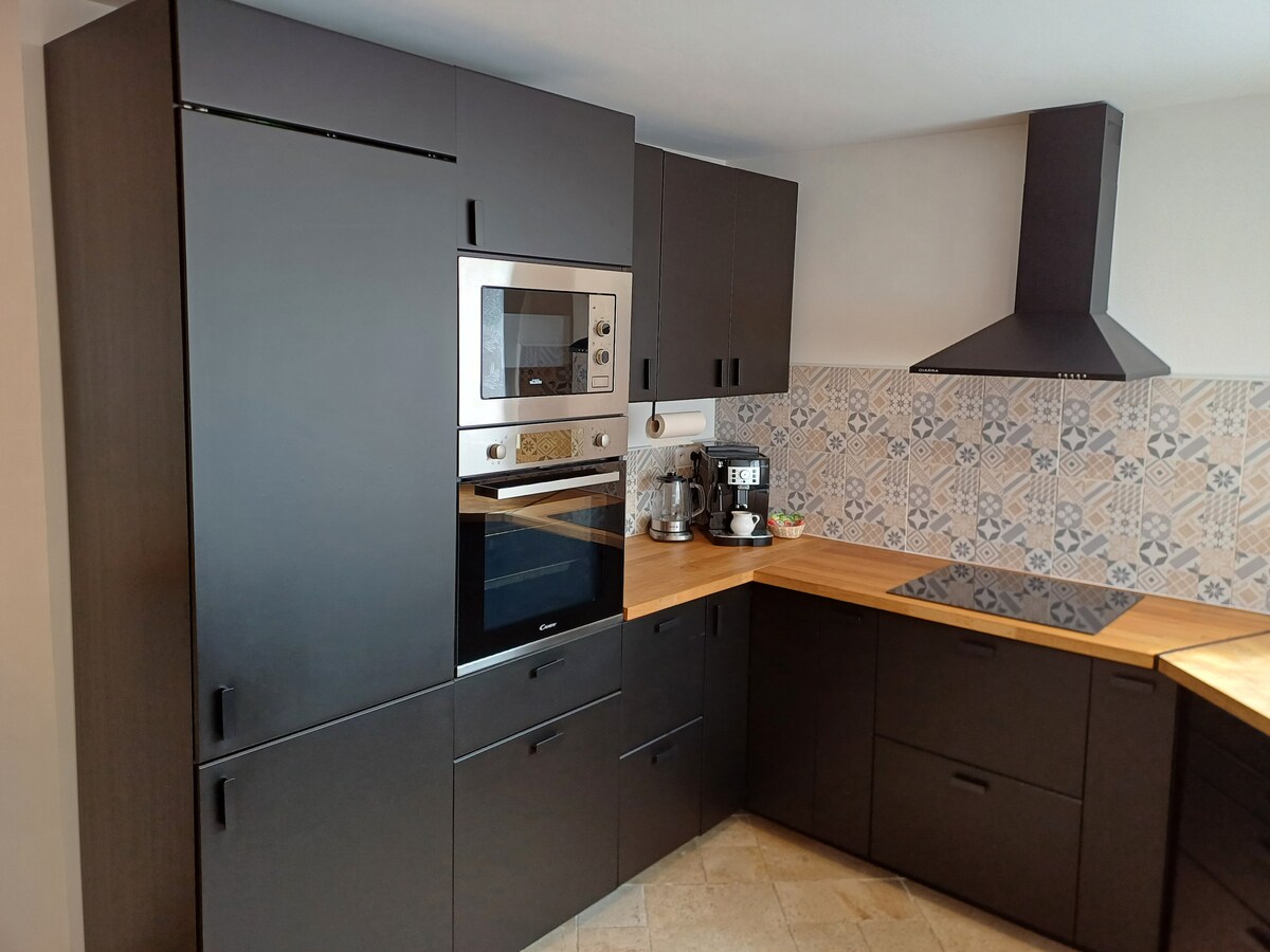 A modern kitchen setup features sleek dark cabinetry with a wooden countertop. Built-in appliances, including an oven and microwave, are present. Decorative tiles adorn the backsplash, adding a subtle pattern. Ample counter space is available for meal preparation and serving.