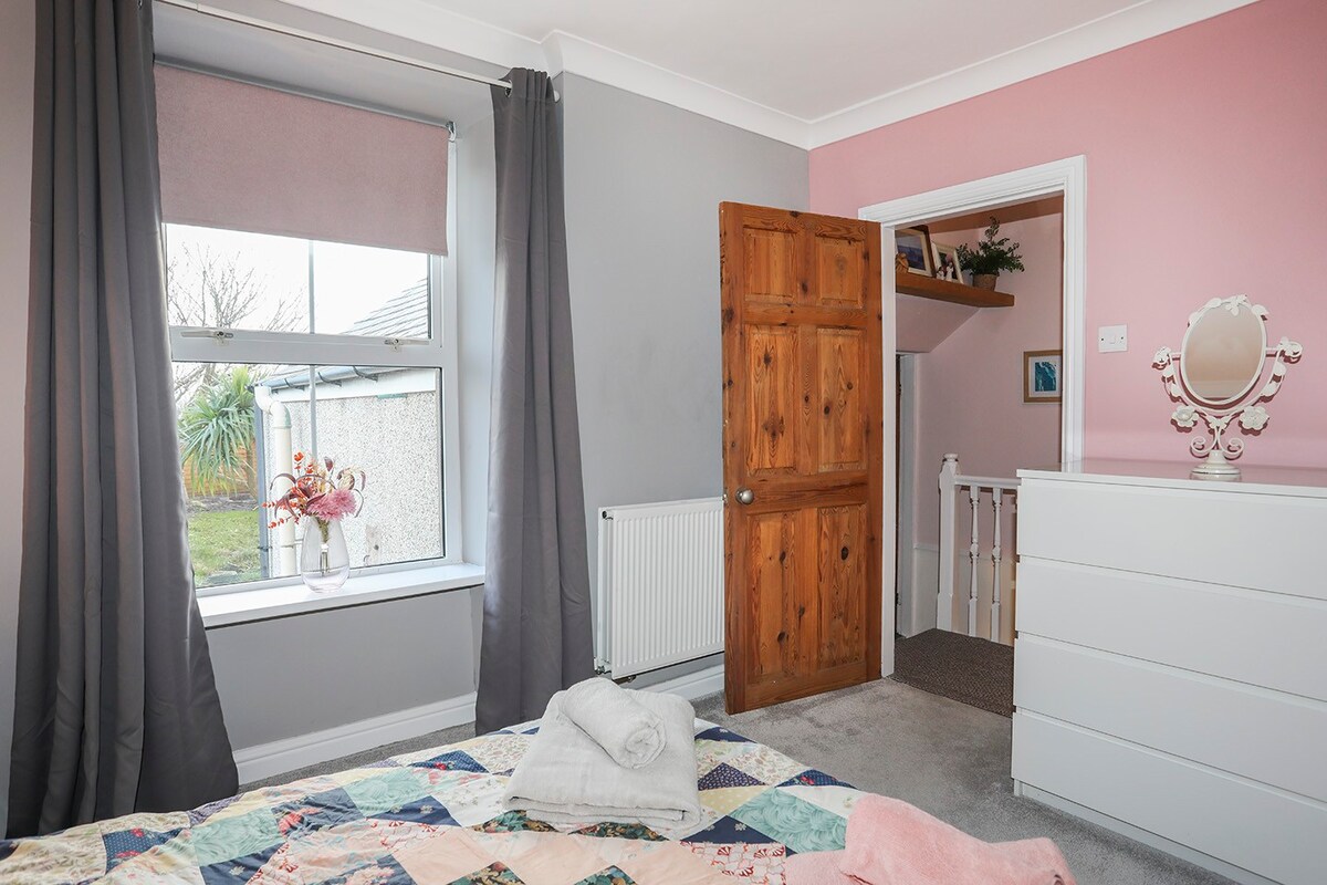 Ორადგილიანი საწოლი, რომელიც გადაჰყურებს ბაღს სათავსოთი, თეთრეულითა და ფენით. 