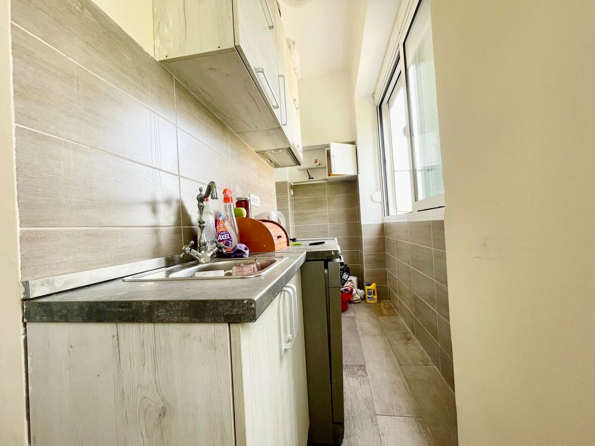 The kitchen showcases modern cabinetry with a blend of light and dark finishes. A dual-basin sink is accompanied by countertop space, while essential appliances are positioned nearby. Natural light enters through a large window, creating a bright and functional cooking area.