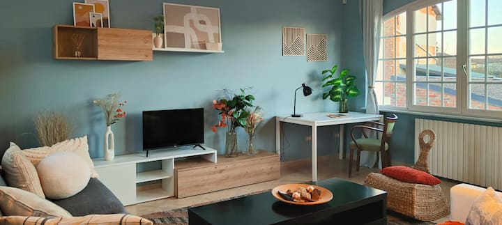 The living room has a comfortable double sofa bed, Smart TV, and a smart working station. Fast Wi-Fi ensures stable connections, and large windows offer natural light. Blackout curtains for privacy and comfort. 