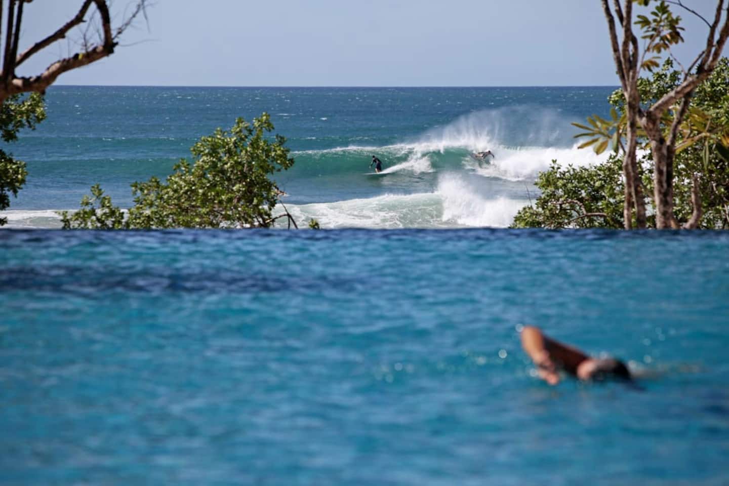 A surfer in the waves at Playa Avellanas, seen from the Beach Club’s infinity pool