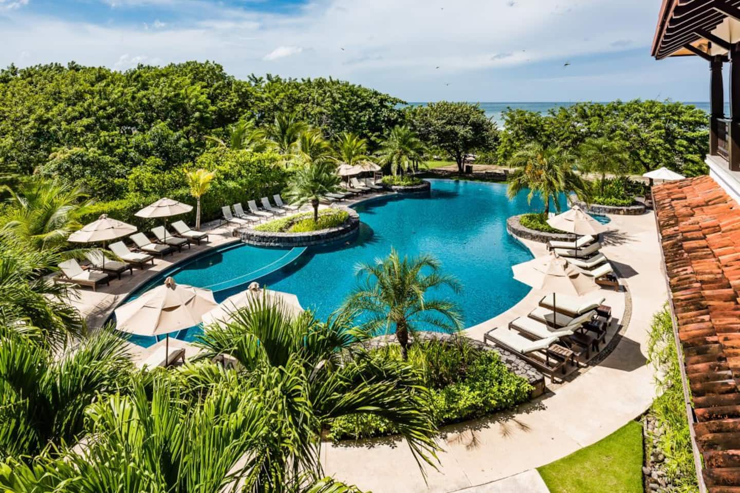 The Hacienda Pinilla Beach Club pool among palms, with loungers and umbrellas