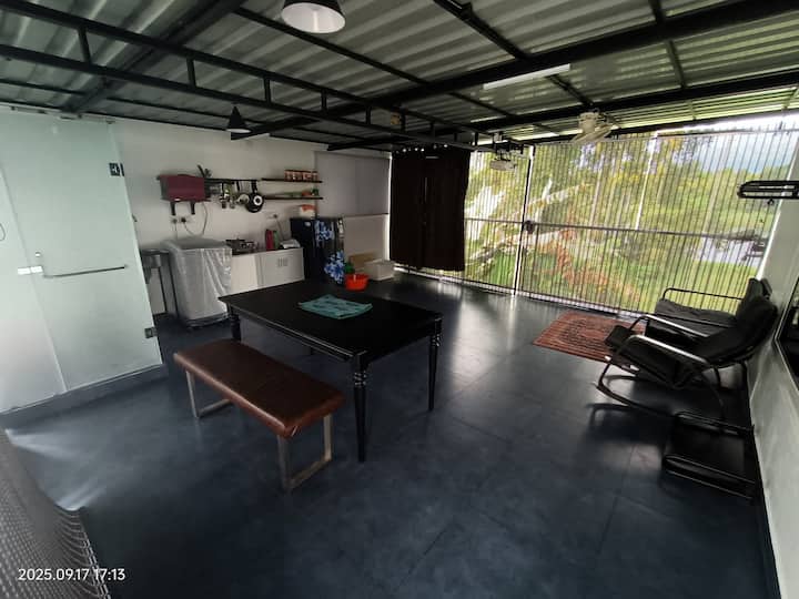 Salon, salle à manger et garde-manger. Semi-ouverte. Contient des équipements de cuisine : plaque de cuisson, ustensiles, couverts, réfrigérateur, micro-ondes, grille-pain, lave-linge. Mini toilettes avec douche. Table à manger. Projecteur avec smart box pour visionner le contenu OTT. Ventilateurs