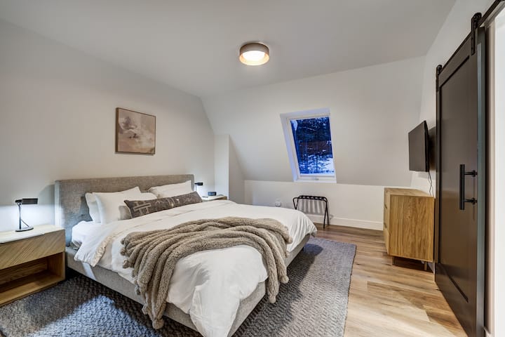 King guest bedroom-ensuite bathroom, located on the main floor. Plush bedding and carpet, plenty of storage with dresser and closet space.  This is the coziest room in the house! Large window and view of the pine trees. Streaming TV mounted on wall.