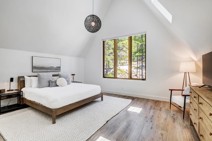 Primary suite includes plush bedding and area rug; custom electric blackout shades and modern decor. Streaming TV and phone chargers on nightstands. Closets and ensuite bathroom with robe and slippers. Complete privacy and quiet. 
