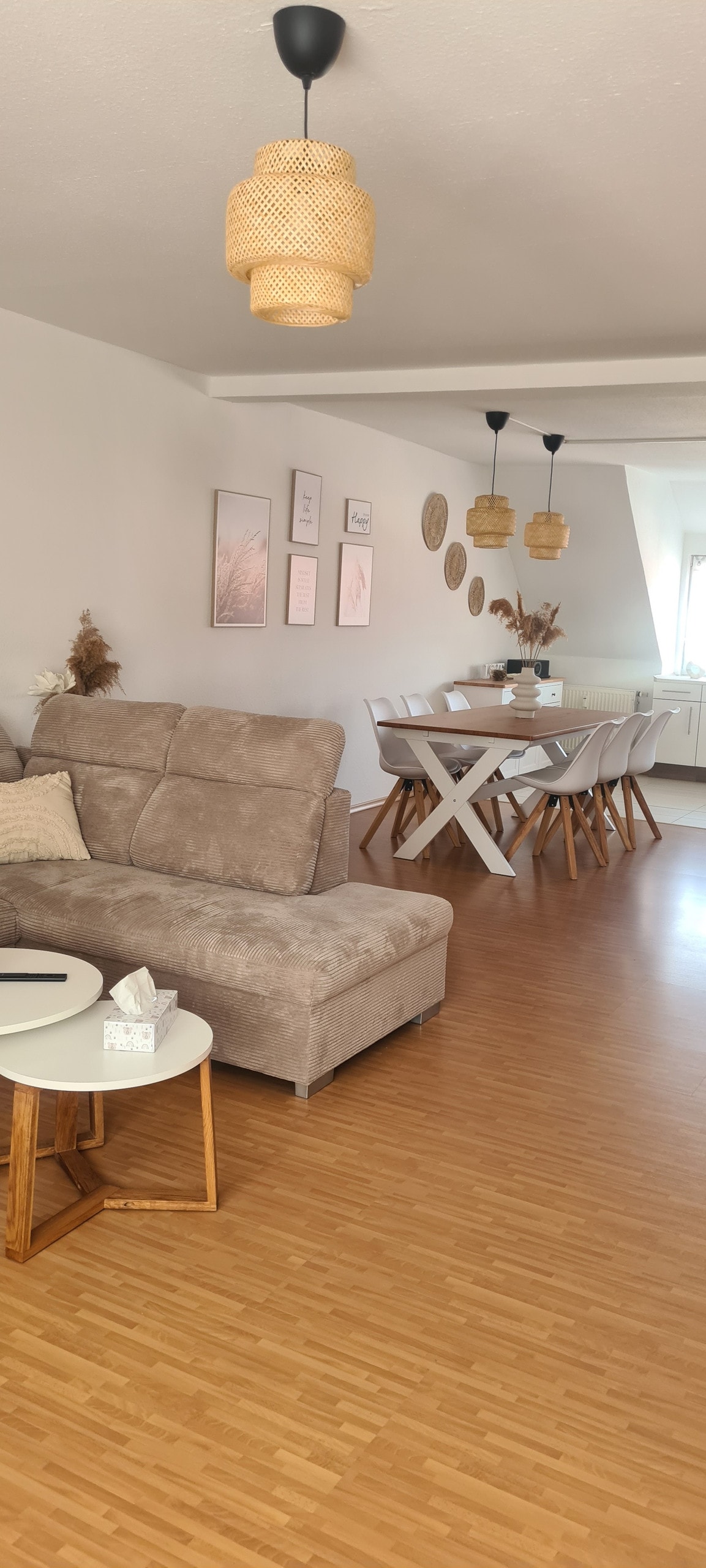 A spacious living area is furnished with a light-colored sofa and a small wooden side table. Light oak flooring is complemented by a modern dining table with wooden chairs. Soft, muted decor adorns the walls, contributing to a harmonious atmosphere.
