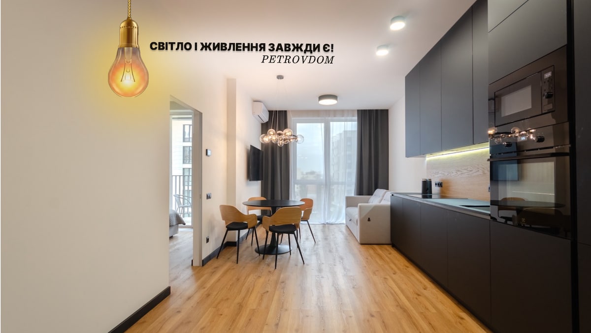 A modern kitchen area is showcased, featuring sleek black cabinetry and a built-in oven. A dining table with four chairs is placed nearby, while large windows provide natural light and access to the balcony. The warm wood flooring adds a comforting touch to the space.
