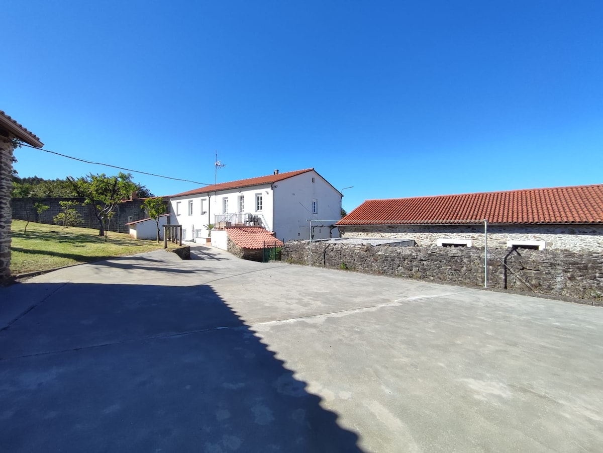 A spacious outdoor area featuring a concrete surface is shown, with a two-story building in the background. The building's white exterior is highlighted against a clear blue sky, while traditional red-tile roofs indicate the style of the surrounding structures.