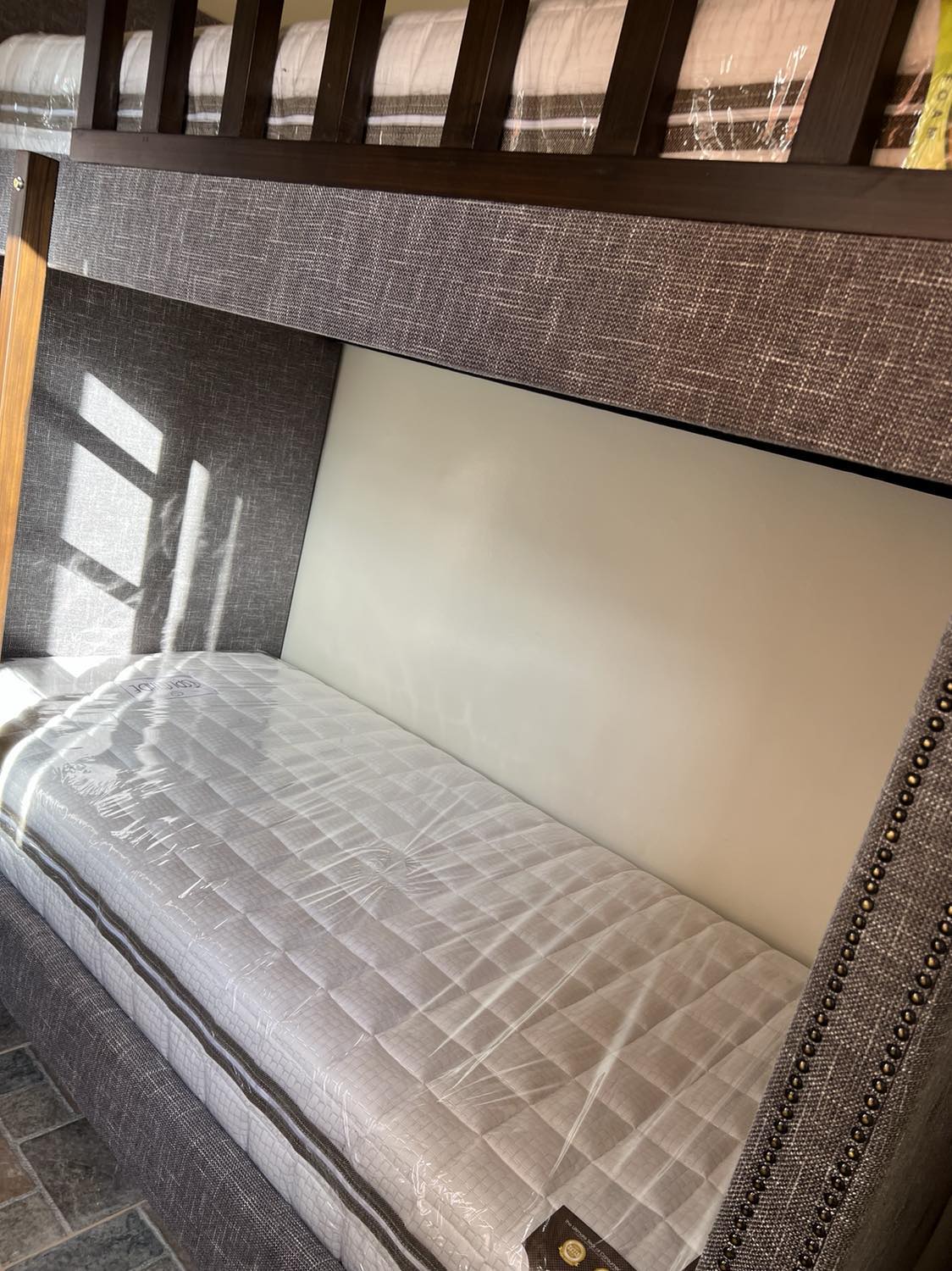 A compact sleeping area is featured, with a cushioned mattress positioned against a neutral wall. Natural light filters in, casting soft shadows on the surface. The bedding is neatly arranged, providing a tidy and inviting space for rest.