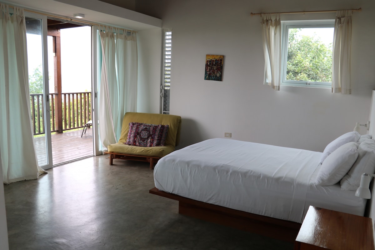 Studio apartment with a comfortable queen bed and a twin futon. The unit has a ceiling fan above the bed and plenty of ventilation. 