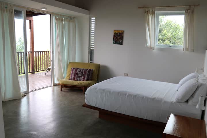 Studio apartment with a comfortable queen bed and a twin futon. The unit has a ceiling fan above the bed and plenty of ventilation. 