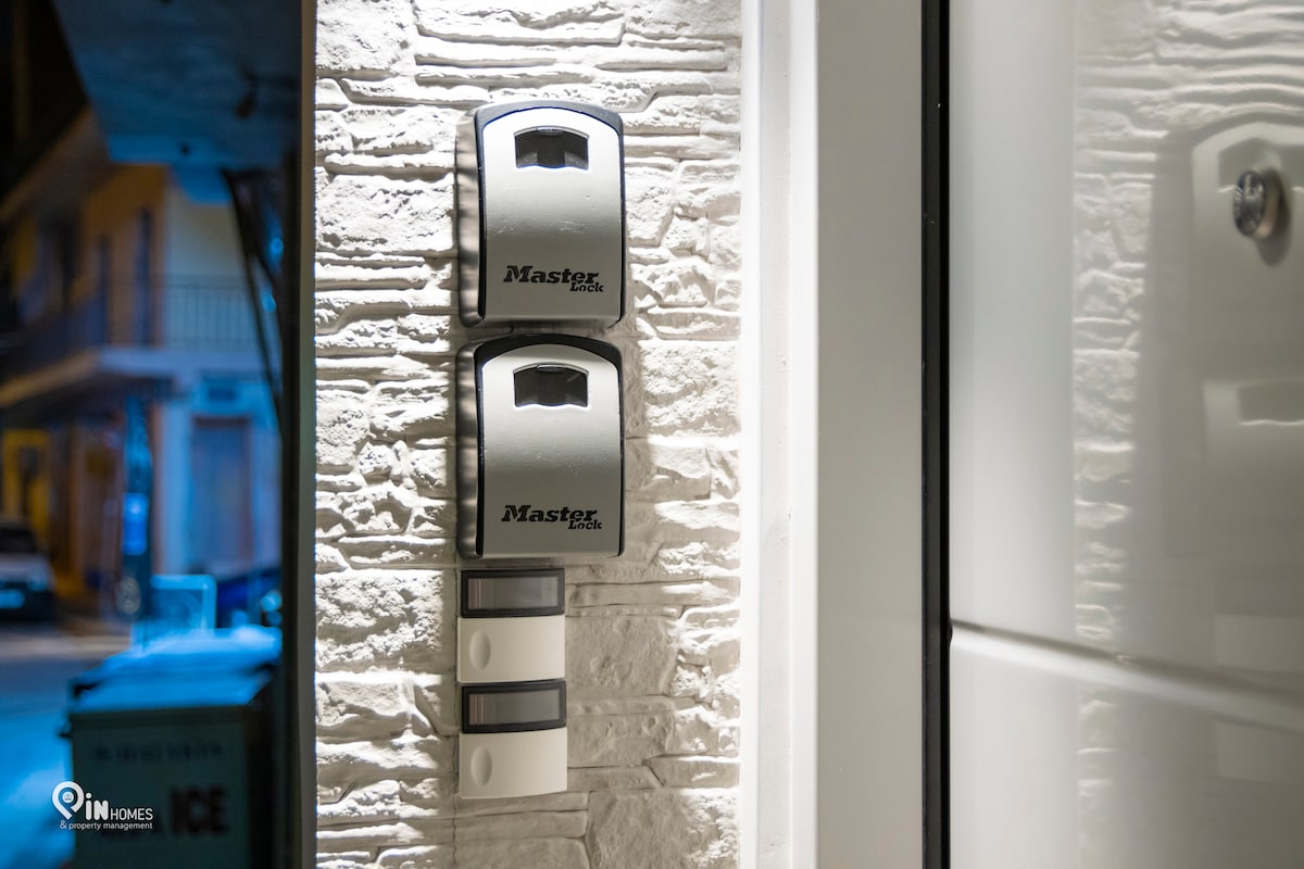 Two mailbox units are mounted on a textured stone wall, featuring a modern design. Below the mailboxes, a white panel houses three intercom buttons, positioned conveniently for easy access. The scene is softly illuminated, enhancing visibility during nighttime.