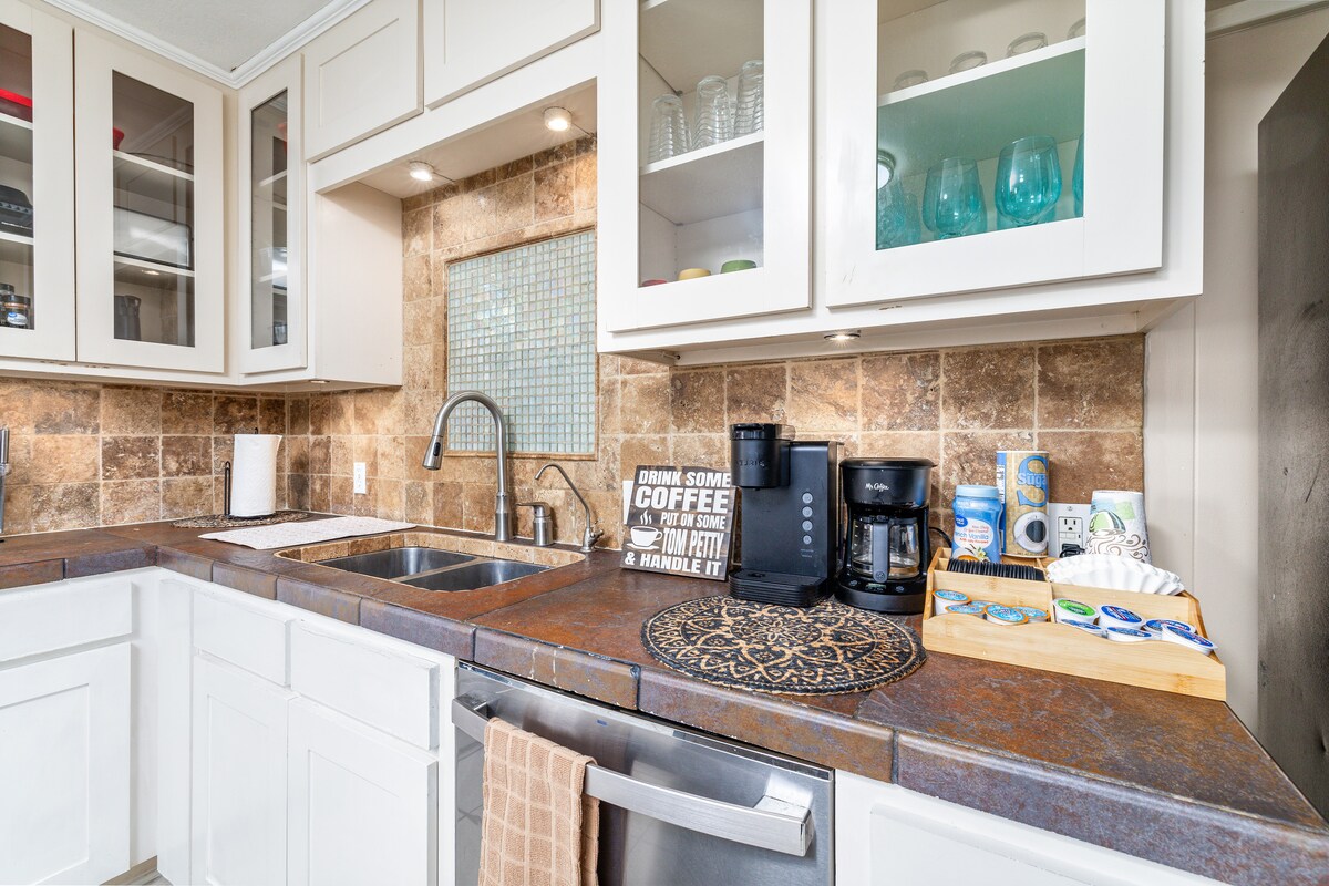 A modern kitchen is displayed with sleek cabinetry and a variety of organized kitchenware. An under-cabinet light illuminates the workspace, while a coffee maker and a selection of condiments are positioned on the counter, providing a functional and inviting cooking environment.