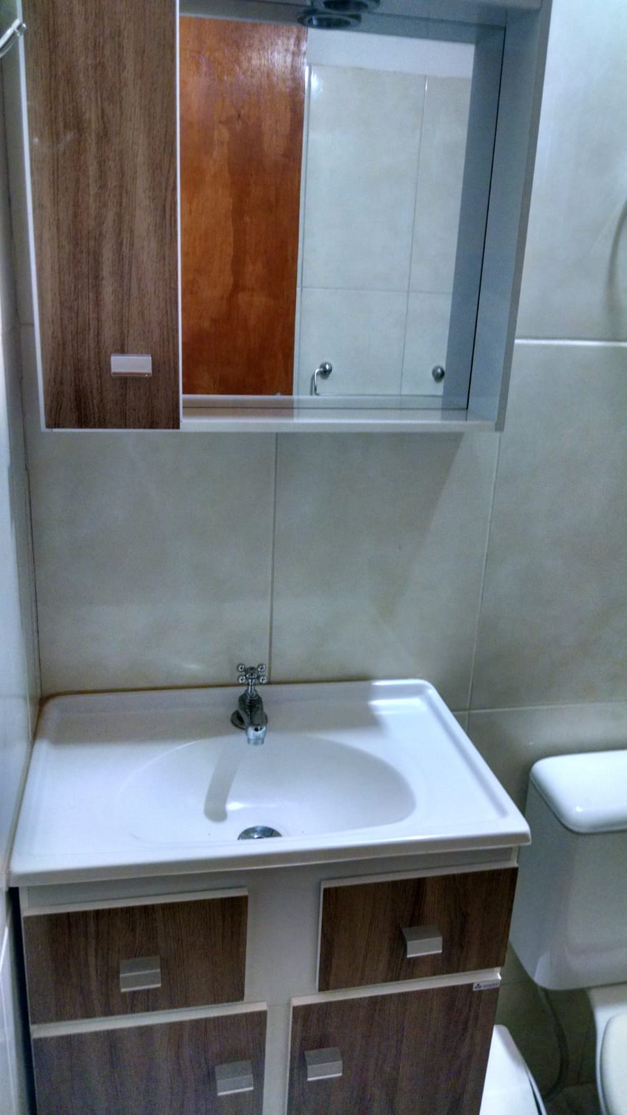 A compact bathroom is visible, featuring a white sink with a modern faucet positioned above a storage cabinet. A mirror is mounted above the sink, and a light-colored tiled wall adds brightness to the space. A toilet is discreetly placed to the side.