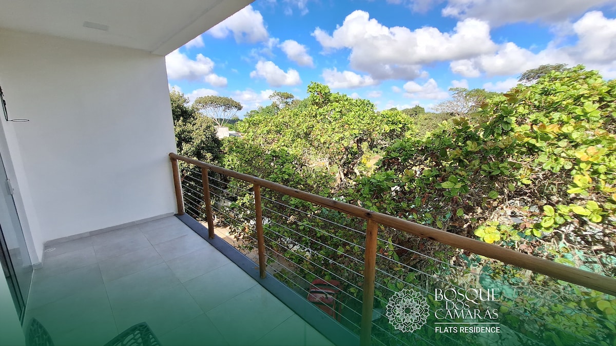 A spacious balcony features wooden railings and offers a view of lush greenery, with trees and a blue sky dotted with clouds in the background. The tile flooring adds a clean and modern touch.